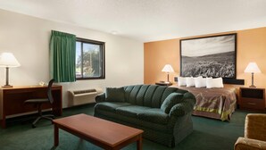 A hotel room with a bed, a green sofa, a wooden desk, two lamps, and a large landscape painting on the wall. - Super 8 by Wyndham Concordia (Concordia)