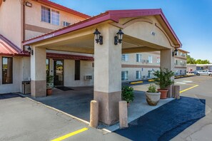 A hotel entrance with a covered patio, potted plants, and a clear blue sky.