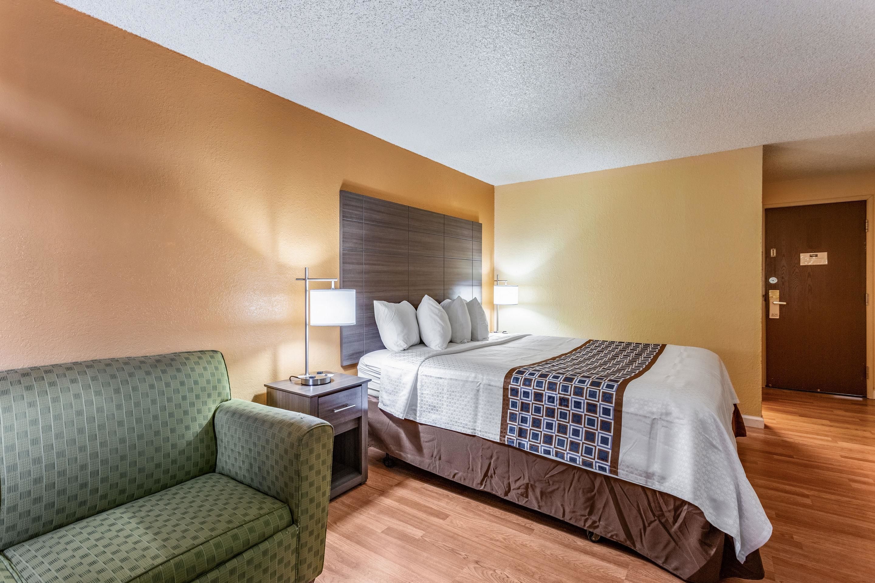 Ein Hotelzimmer mit Bett, Nachttisch, Lampe, Stuhl und Holzboden.