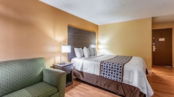 Ein Hotelzimmer mit Bett, Nachttisch, Lampe, Stuhl und Holzboden.