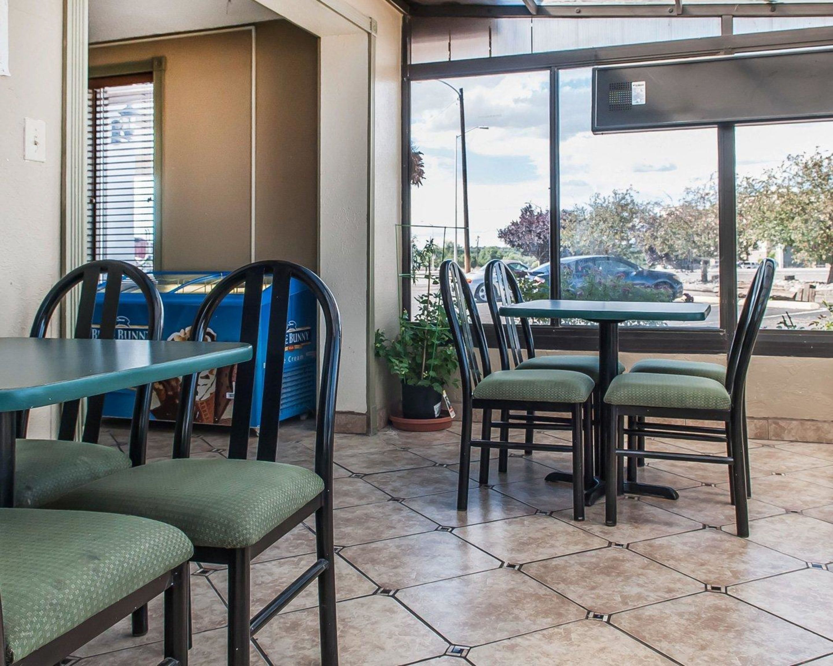 An outdoor seating area with tables and chairs, a blue trash bin, and a view of parked cars through the window.