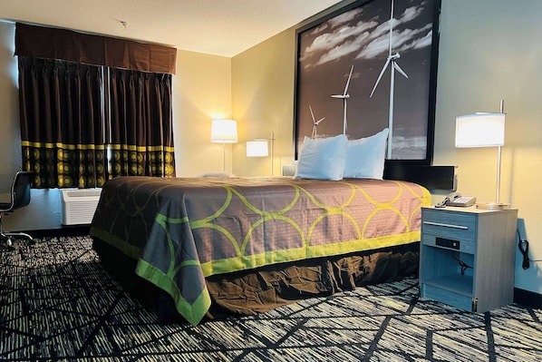 A hotel room with a bed, a desk, a chair, a lamp, and a wall with a wind turbine painting. - Super 8 by Wyndham Pratt (Pratt)