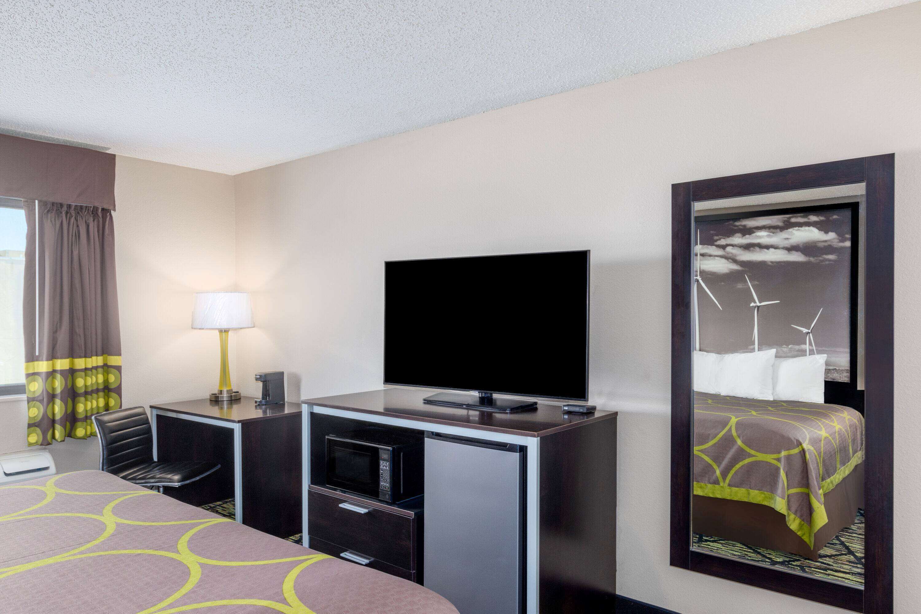 A hotel room with a bed, a desk with a TV, a lamp, a microwave, and a small refrigerator.