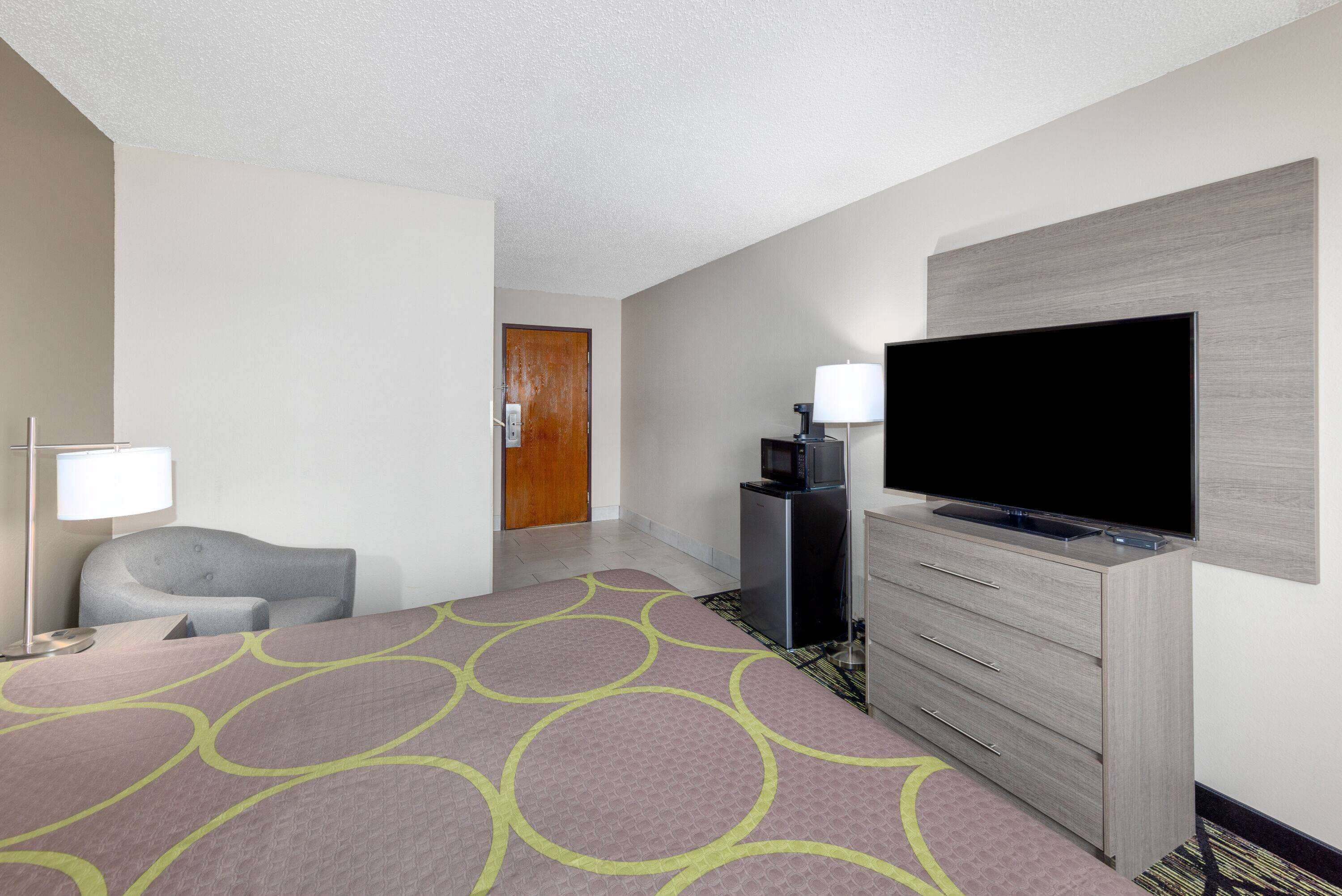 A hotel room with a bed, a TV, a desk, a chair, and a door.