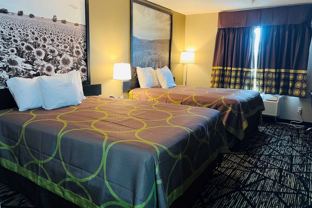 Une chambre d’hôtel avec deux lits, une grande fresque murale et une fenêtre avec des rideaux.
