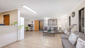 A living room with a sofa, coffee table, and a TV. There is a door leading to another room and a staircase. - Super 8 by Wyndham Pratt (Pratt)