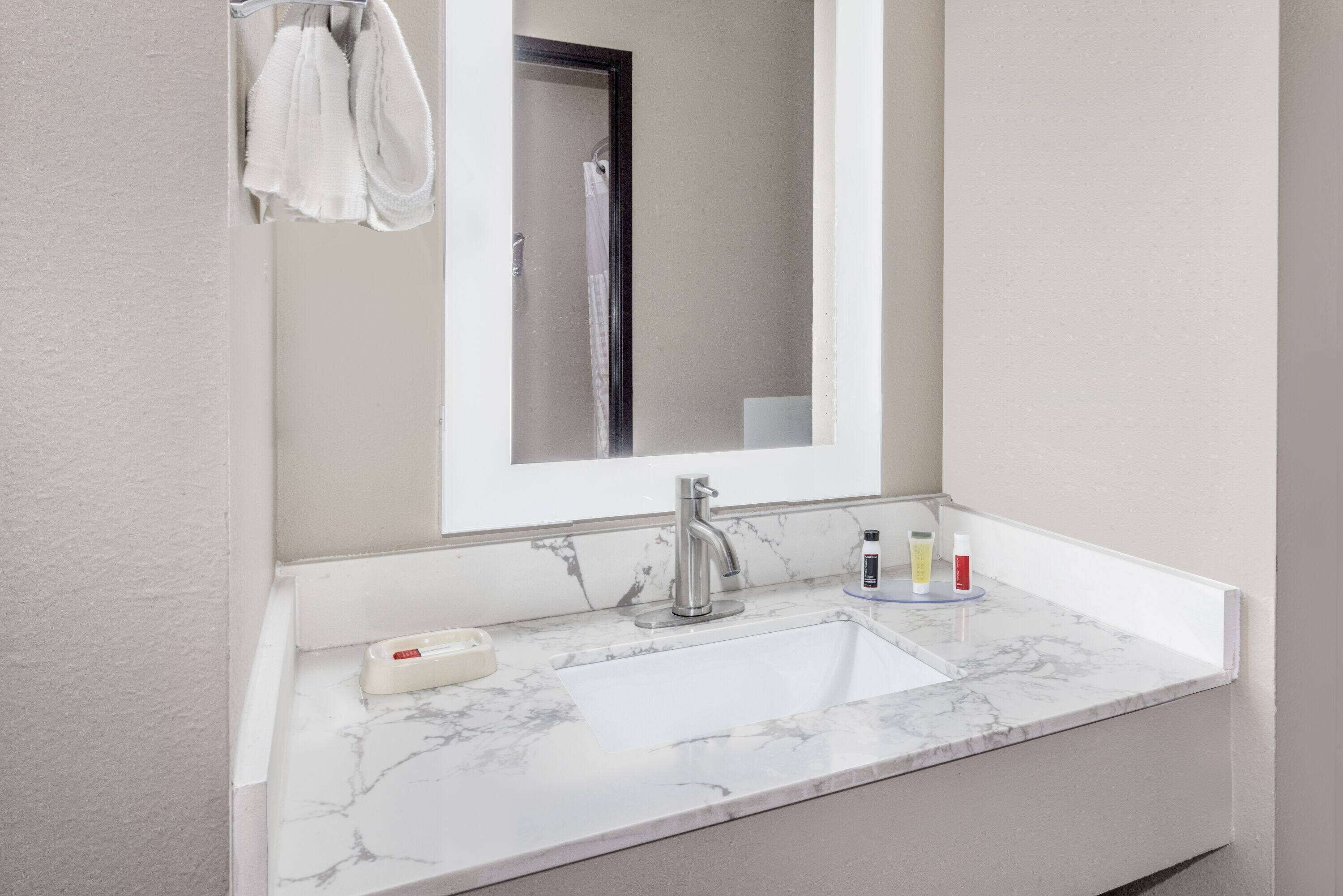 A bathroom with a white marble sink, a modern faucet, and a mirror above it.