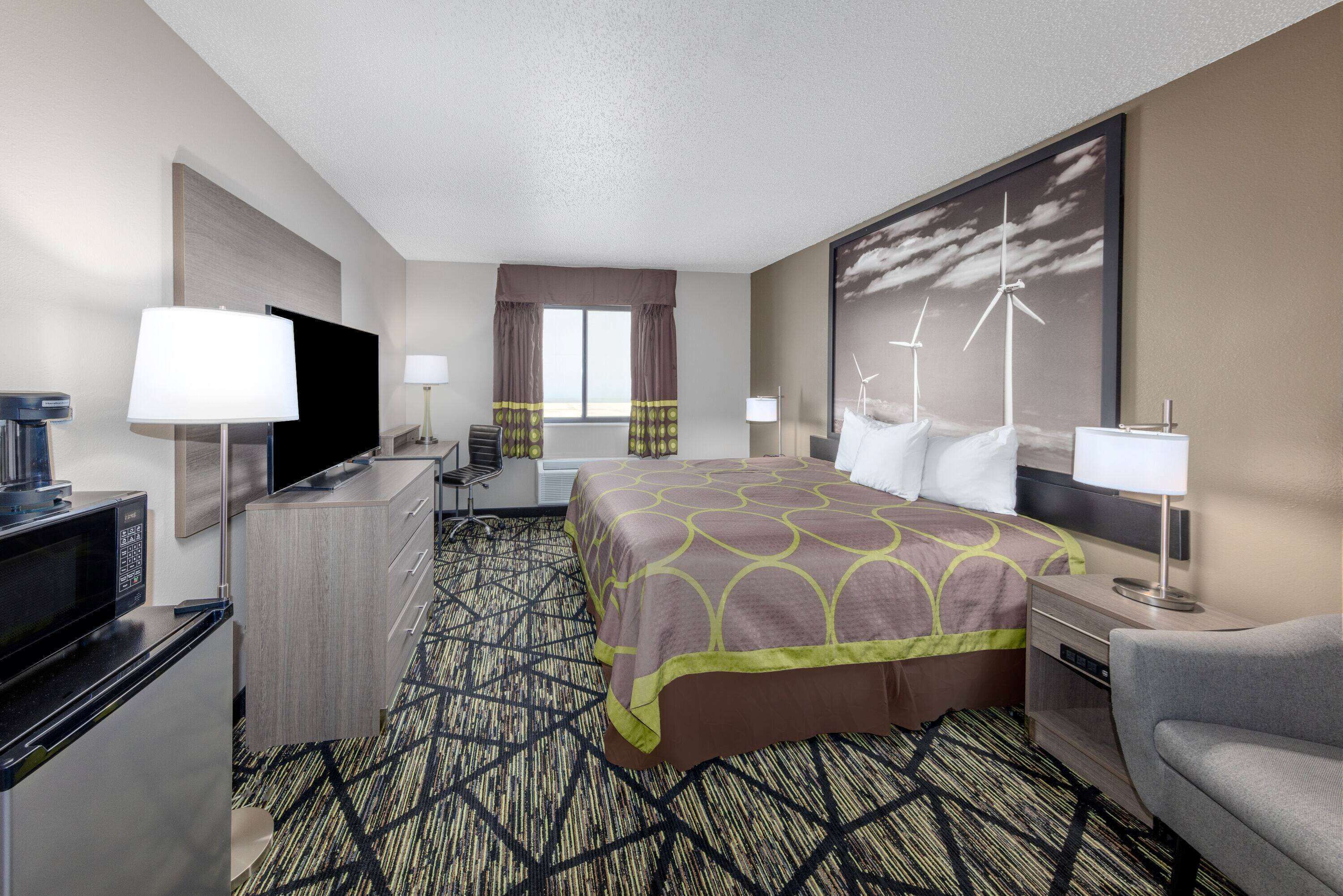 Une chambre d’hôtel comprenant un lit, deux tables de chevet, un téléviseur, un bureau, une chaise et une fenêtre avec des rideaux.