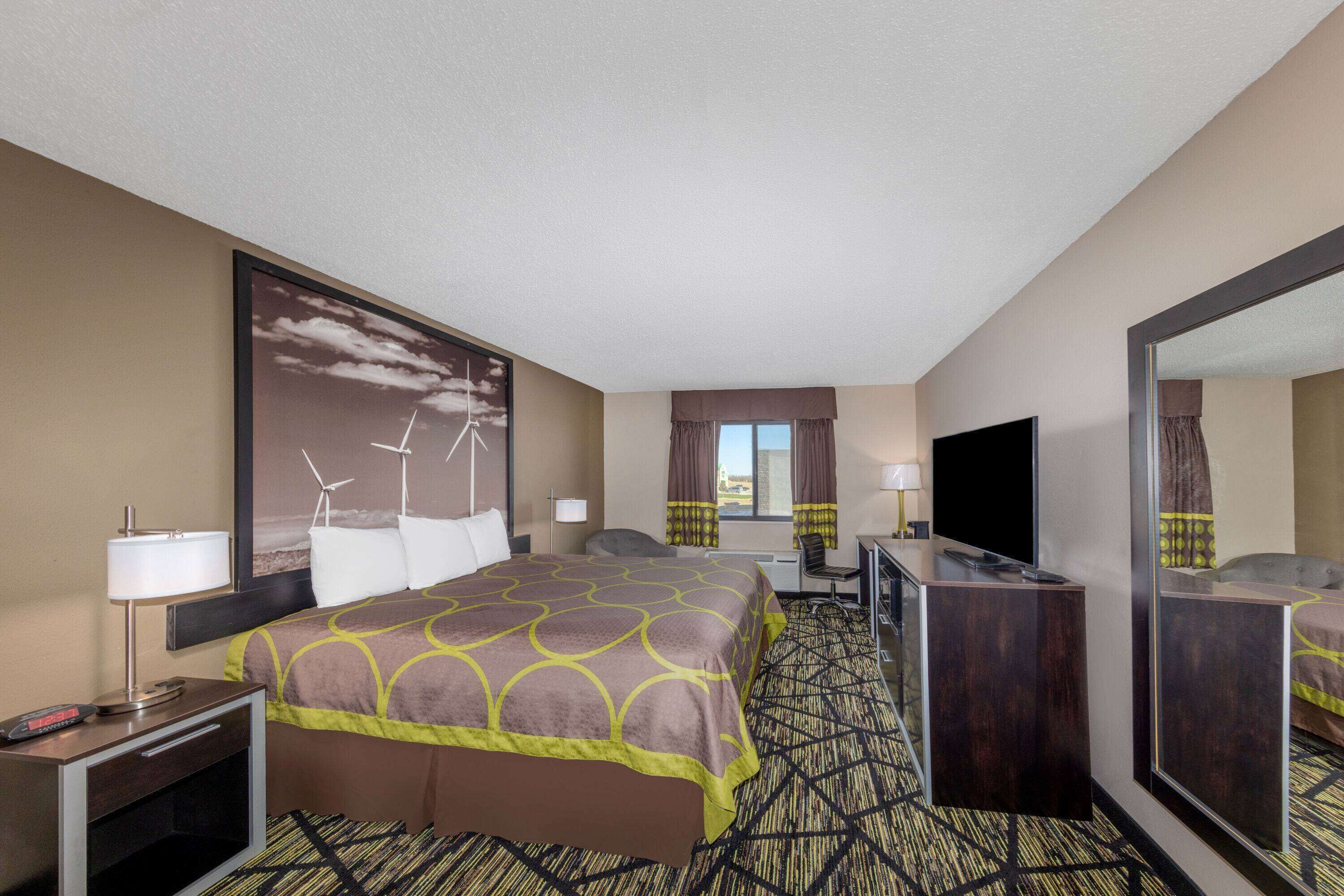 A hotel room with a large bed, a desk, a TV, and a window with curtains.