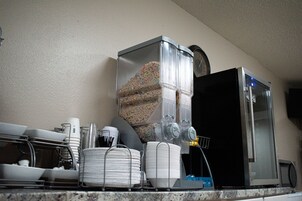 Una cocina con cafetera, refrigerador, y diferentes platos y utensilios.