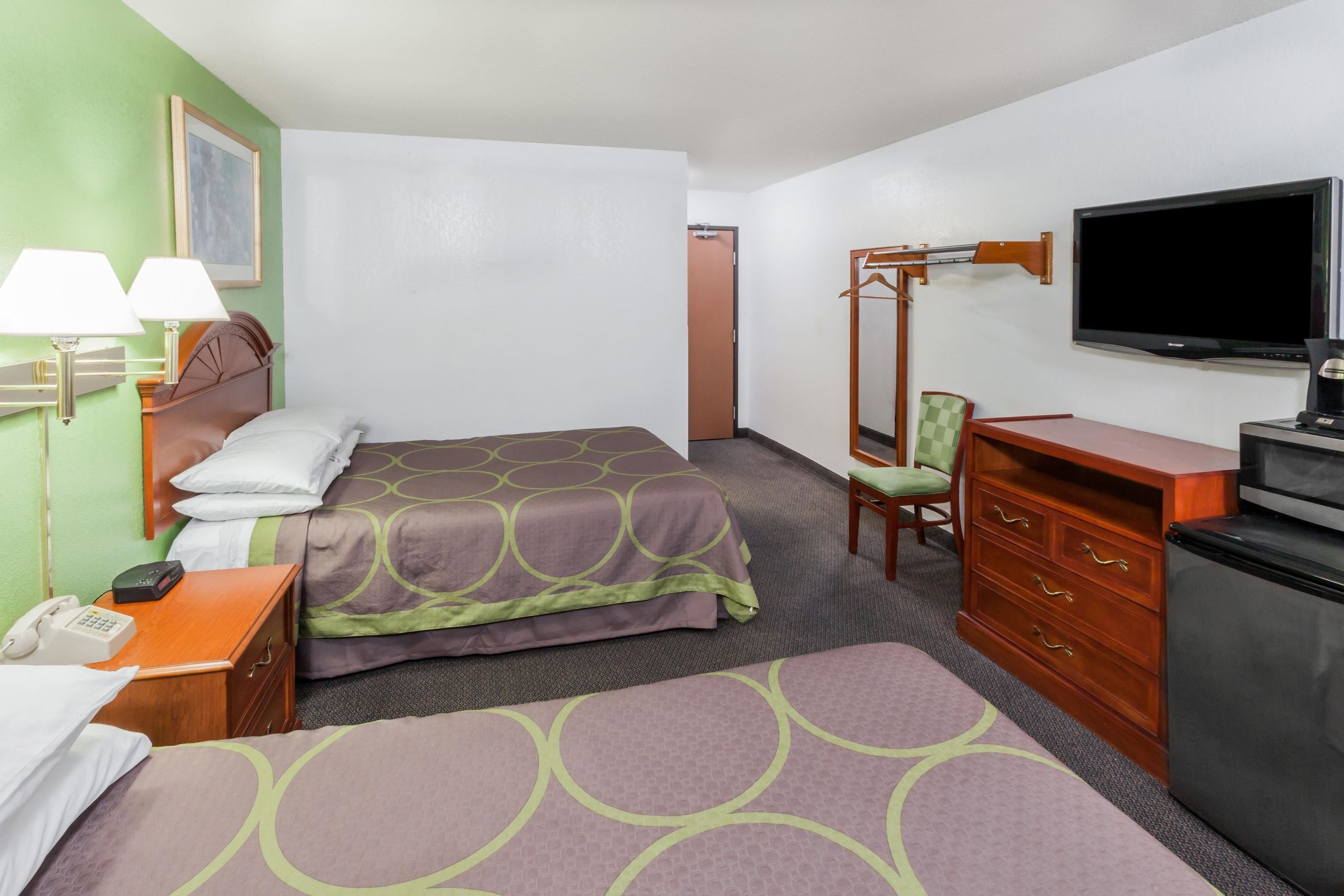 Habitación de hotel con dos camas, televisión, cómoda, una silla y un escritorio con lámpara.