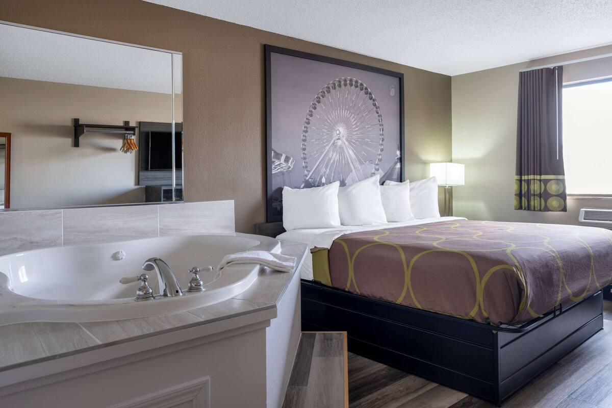 Une chambre d’hôtel avec un grand lit, une salle de bain séparée avec une baignoire et un grand miroir.