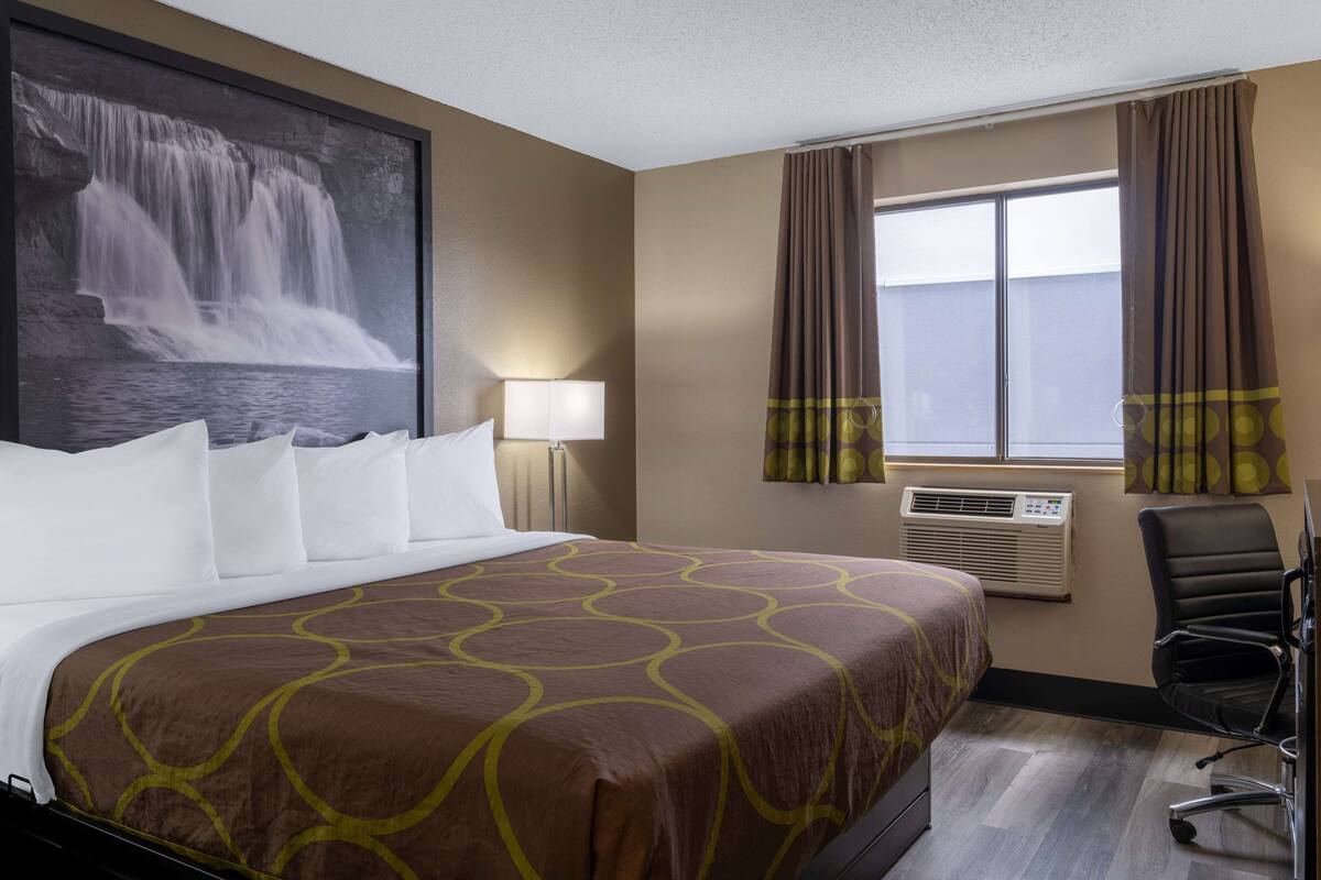 Habitación de hotel con una cama grande, una ventana con cortinas, un equipo de aire acondicionado y una silla.