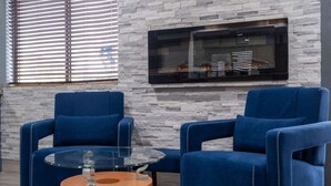 Un salon moderne avec deux fauteuils bleus, une table basse en verre et un mur en pierre.