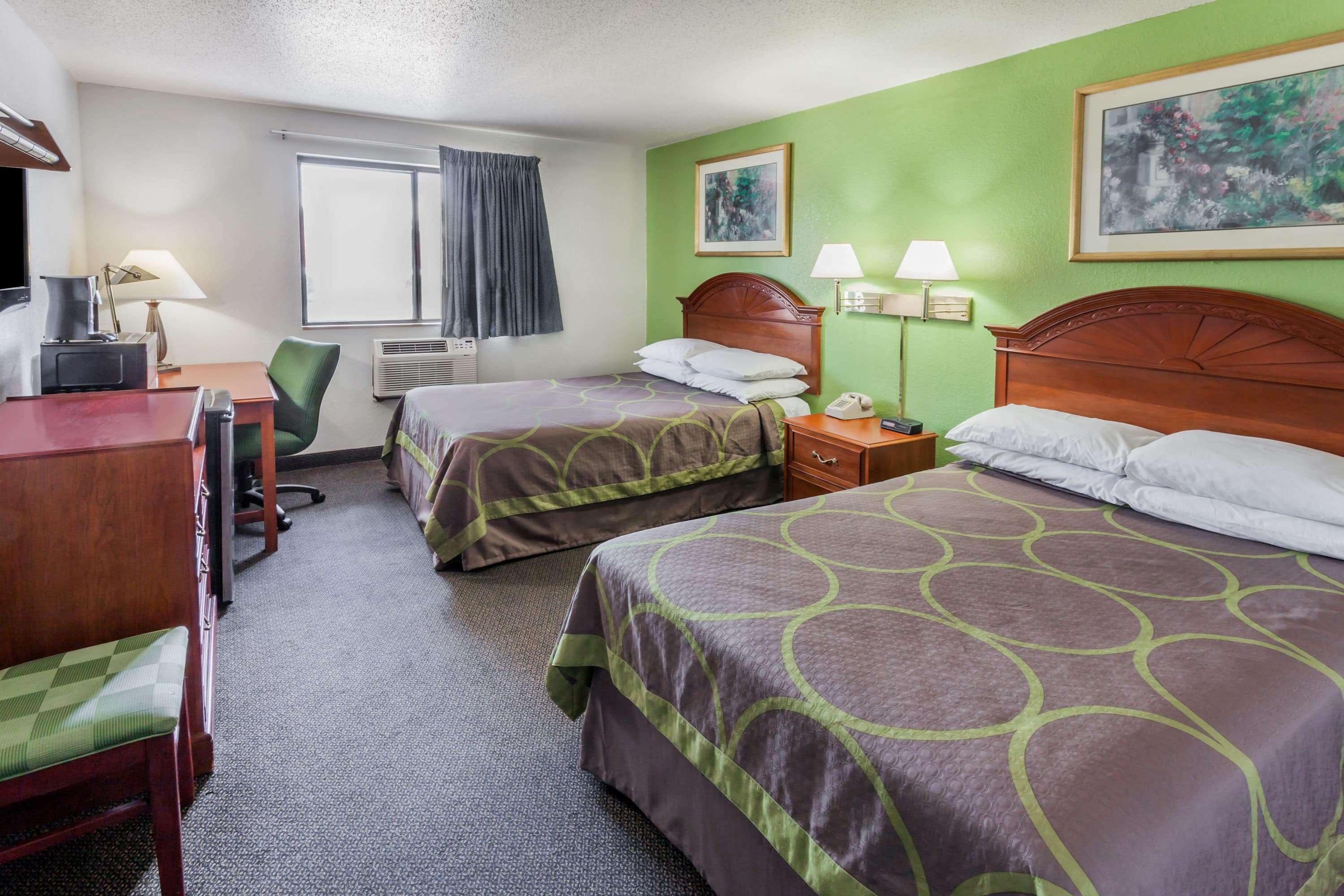 A hotel room with two beds, a desk, a chair, a TV, and a window with curtains.