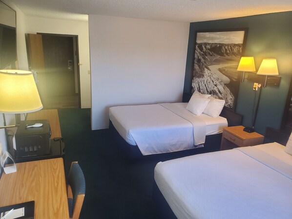 A hotel room with a bed, bedside tables, a desk with a lamp, a phone, and a wall-mounted lamp.