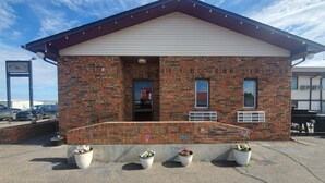 Un bâtiment en briques avec un toit à deux versants, une porte et des fenêtres. Des plantes en pot sont disposées devant.