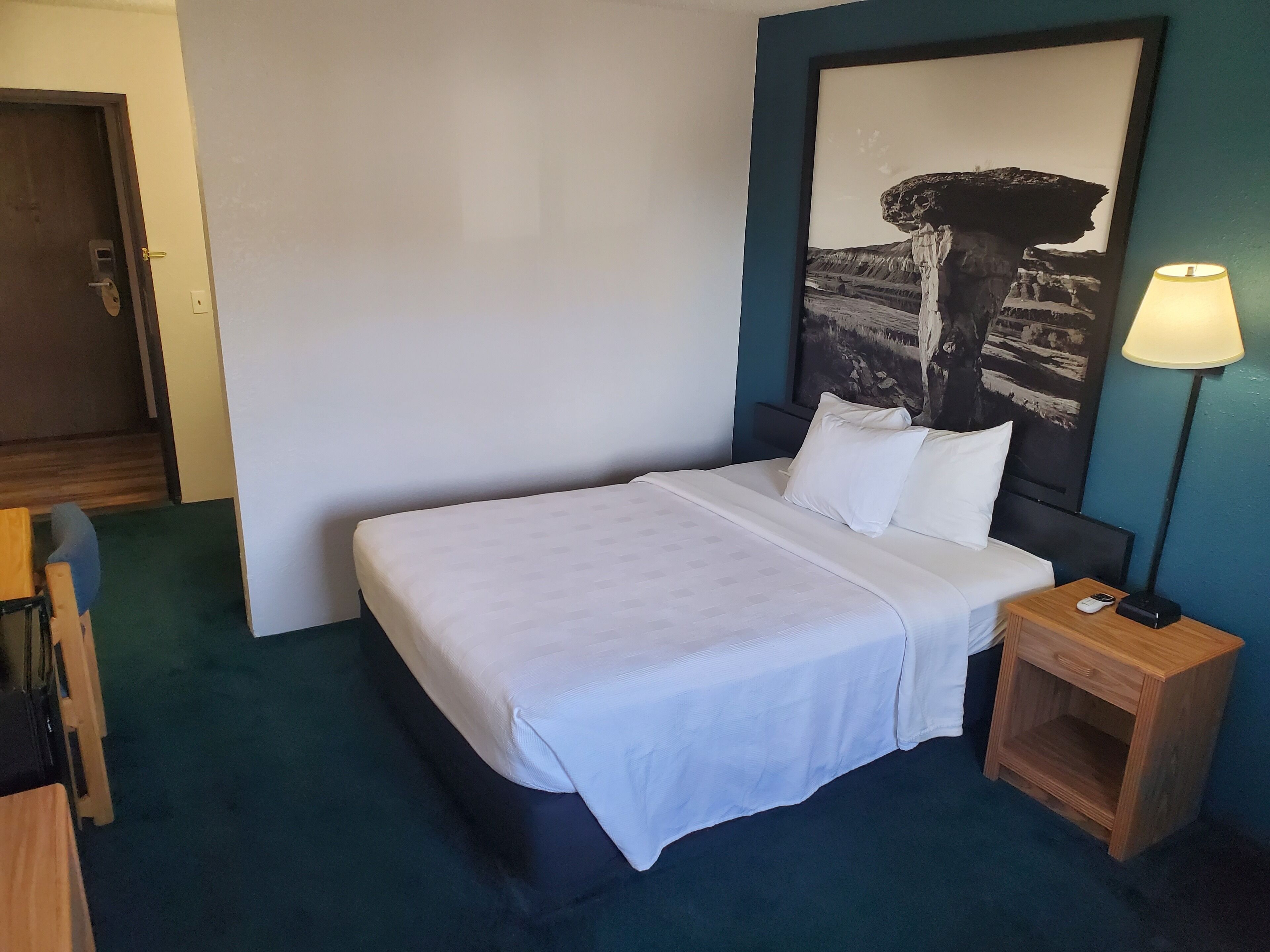 A hotel room with a bed, a nightstand with a lamp, a wooden chair, and a door.