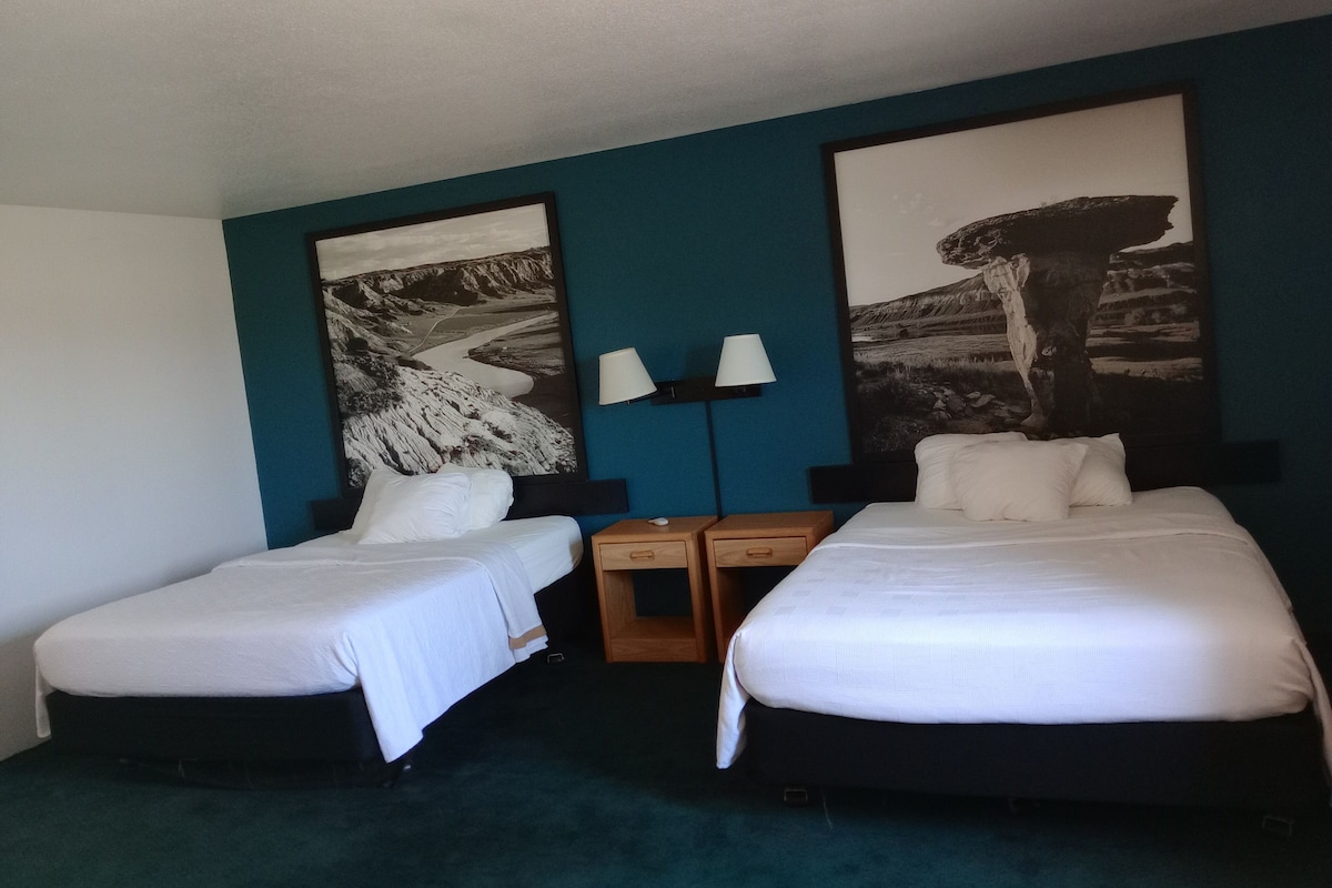 Una habitación de hotel con dos camas individuales, una mesita de noche con una lámpara y dos lámparas de pared.
