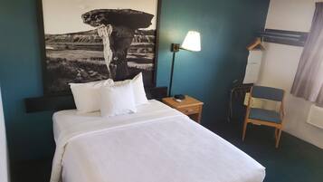 Una habitación de hotel con una cama, una mesita de noche, una lámpara, una silla y un perchero en la pared.