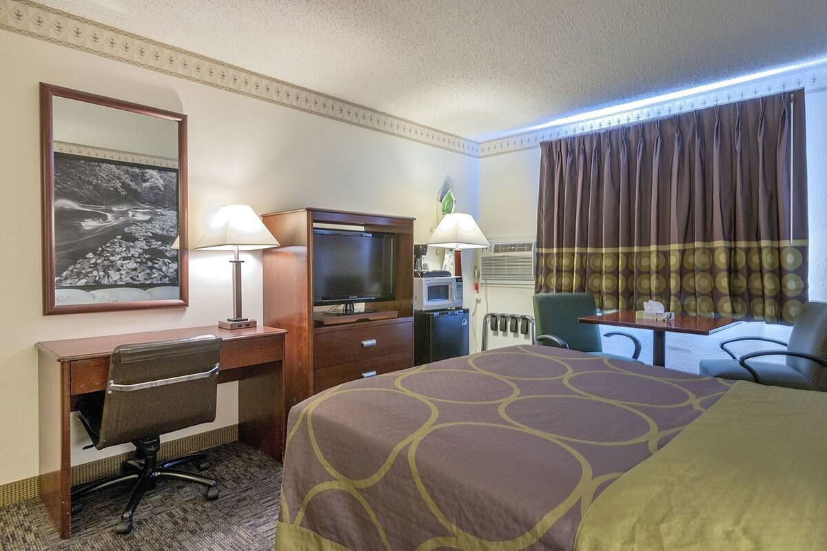 Una habitación de hotel con cama, escritorio, silla, televisor y un cuadro en la pared.