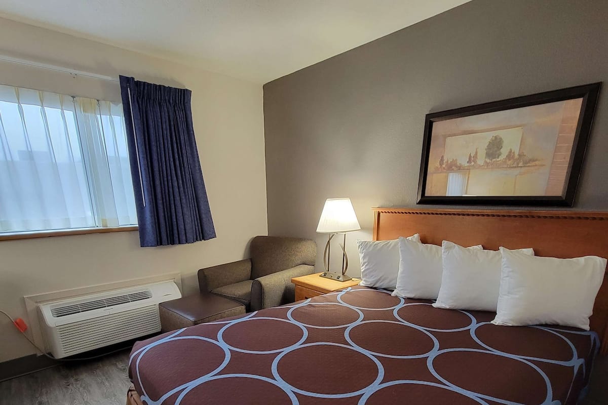 Een hotelkamer met een groot bed, een bureau, een stoel, een lamp en een raam met gordijnen.