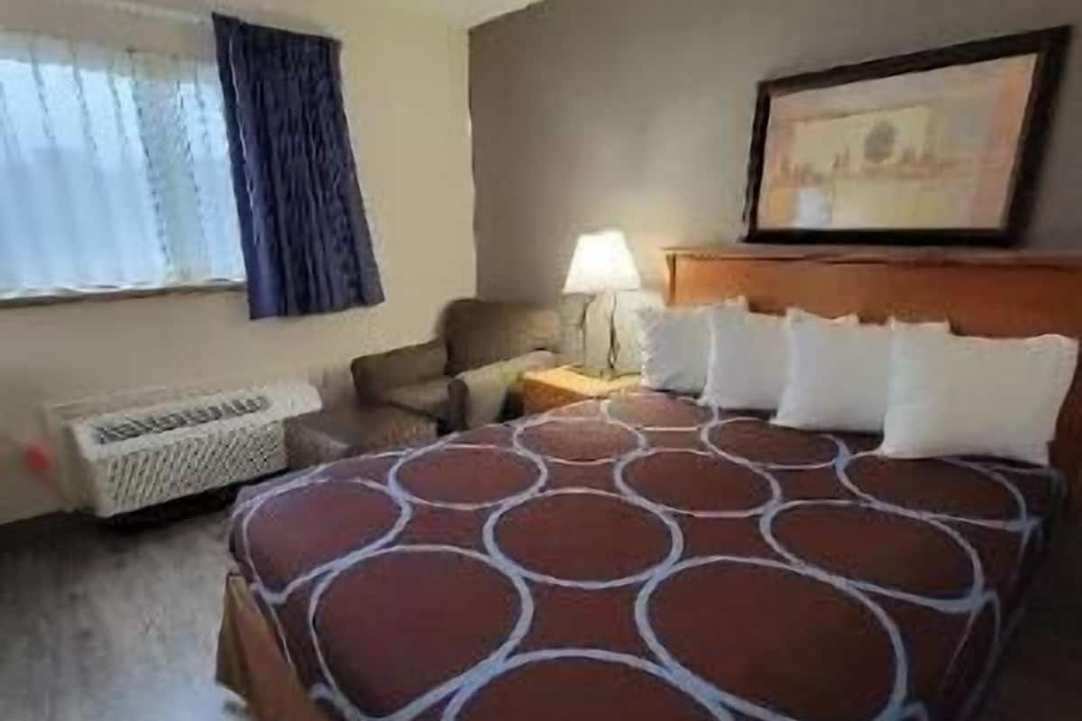 Een hotelkamer met een groot bed, een bureau, een stoel, een raam met gordijnen, een radiator en een ingelijst schilderij aan de muur.