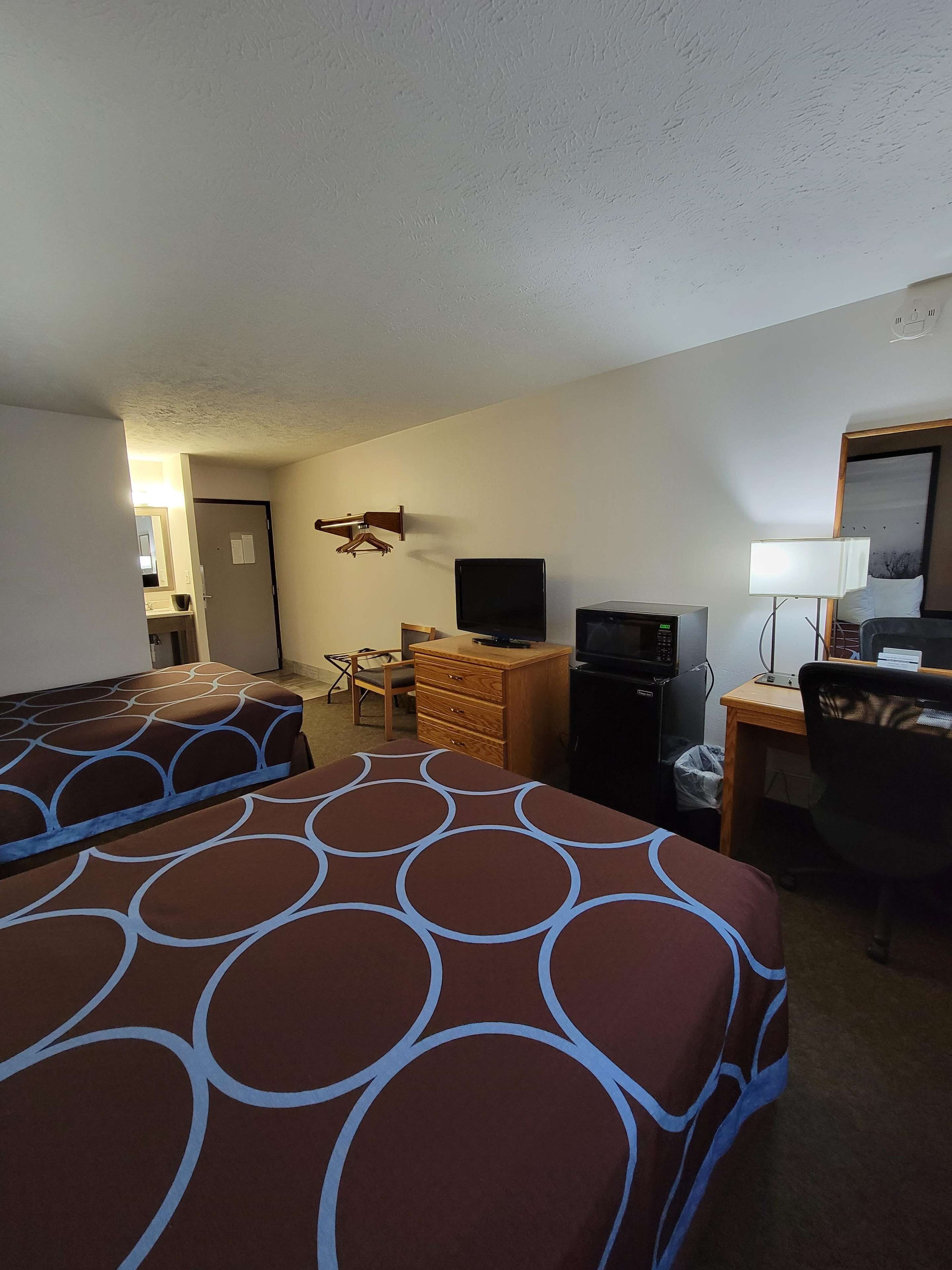 A hotel room with two beds, a desk, a television, a dresser, and a chair.