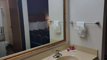 Un baño de hotel con un espejo grande, un lavamanos y un perchero para toallas.