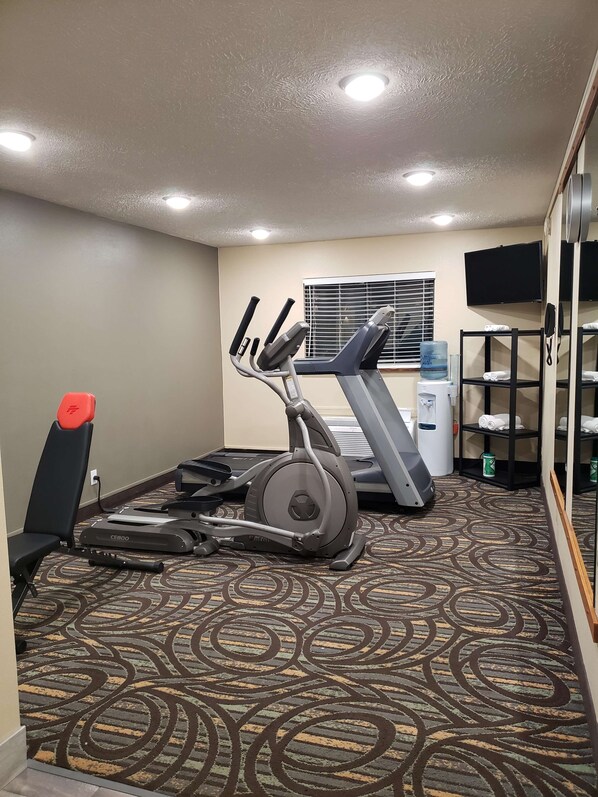 Un gimnasio de hotel con equipo de ejercicio, un dispensador de agua y un televisor en la pared.