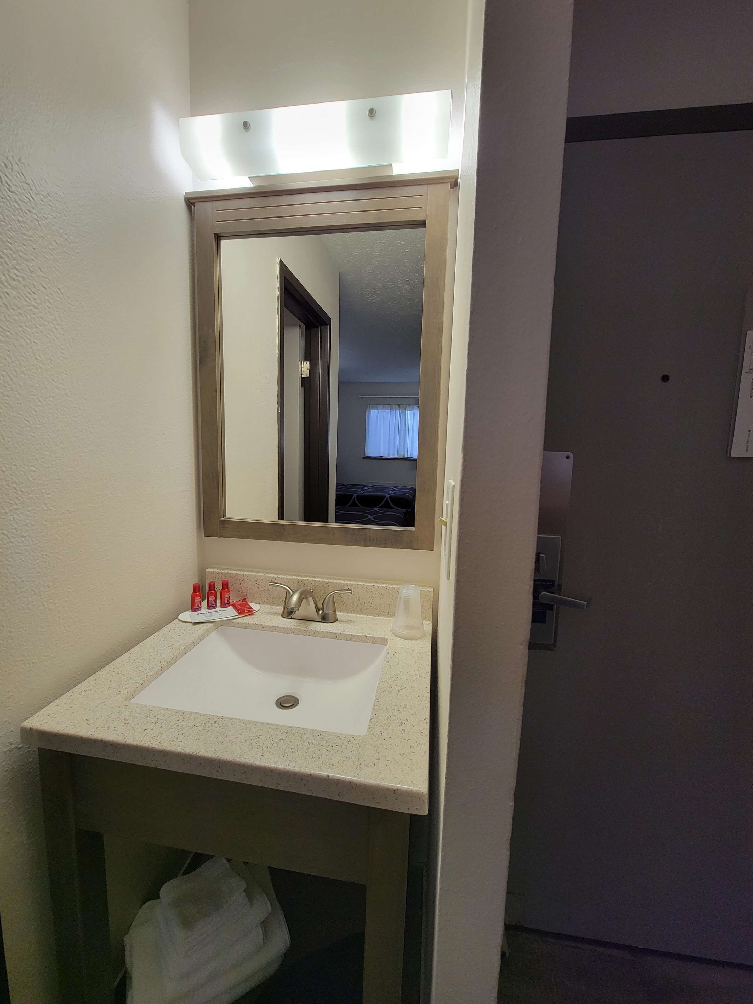 Un baño con lavamanos blanco, un espejo y un perchero para toallas.