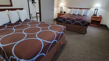 A hotel room with two beds, each with a patterned bedspread, a door, a nightstand with a lamp, and a mirror on the wall.