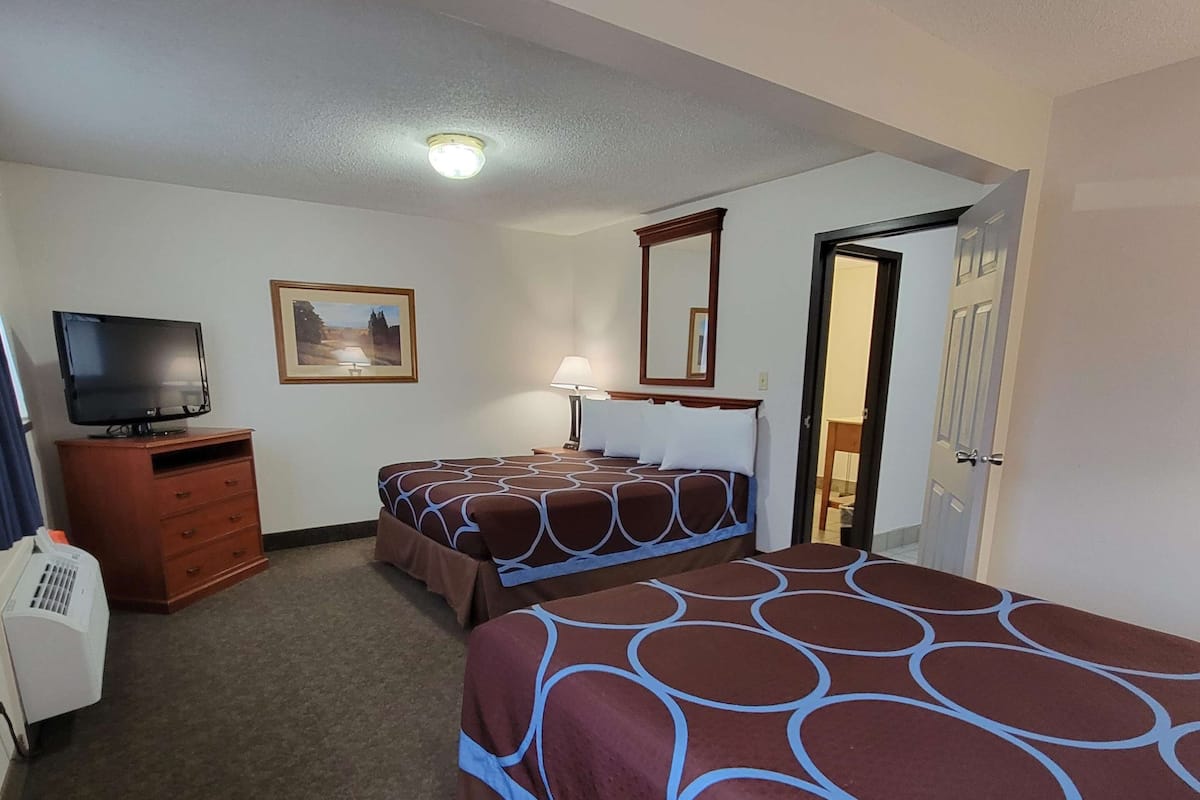 Een hotelkamer met twee bedden, een televisie, een bureau met een lamp en een deur.