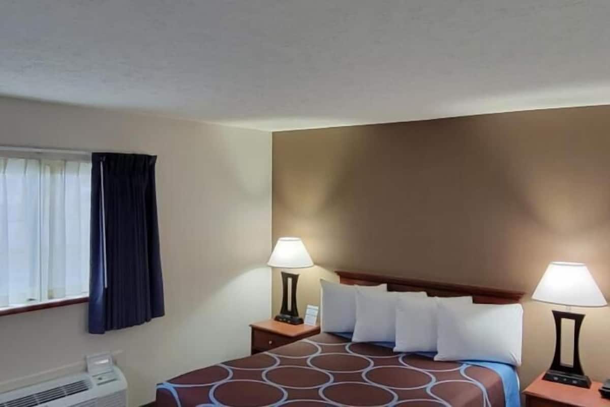 Een hotelkamer met een bed, twee bedlampen, een raam met gordijnen en een heater.