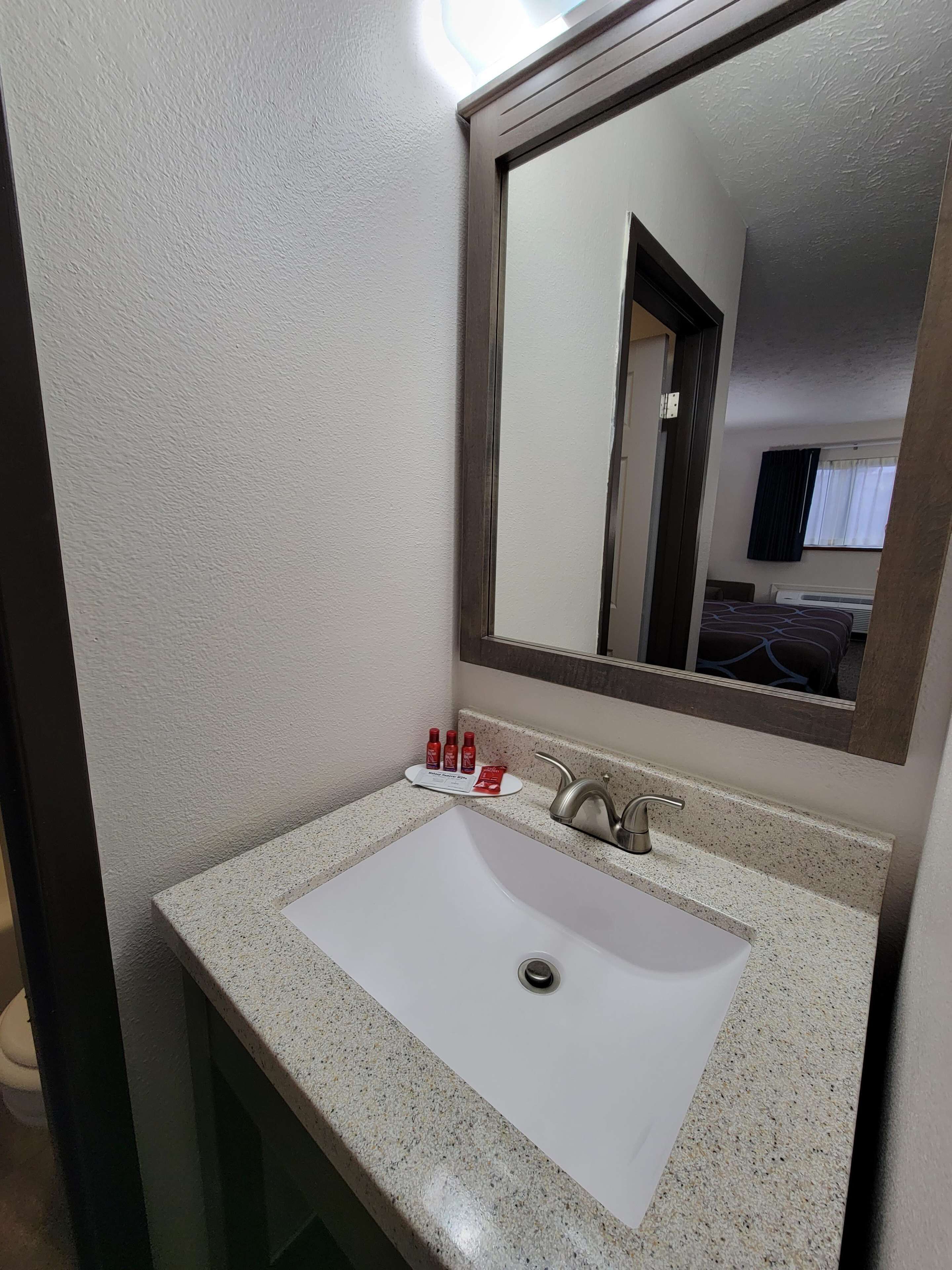 Un baño con lavamanos blanco, un espejo y artículos de aseo en la encimera.