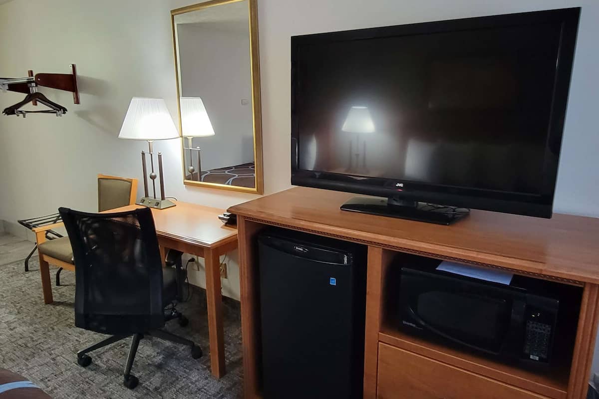 Hotelkamer met een houten bureau, een televisie, een magnetron, een koelkast, een stoel, een lamp en een spiegel.