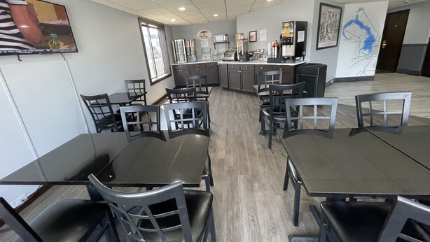 A modern dining area with multiple tables and chairs, a kitchen counter, and a large window. - Super 8 by Wyndham Beaver Dam (Beaver Dam)