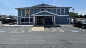 A building with a large garage entrance, a parking lot with marked spaces, and a clear blue sky. - Super 8 by Wyndham Beaver Dam (Beaver Dam)