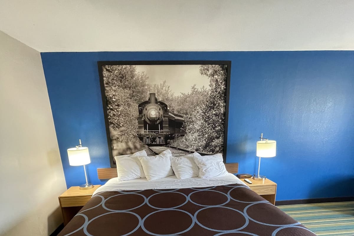A hotel room with a large bed, two bedside tables, and a headboard with a black and white photograph.