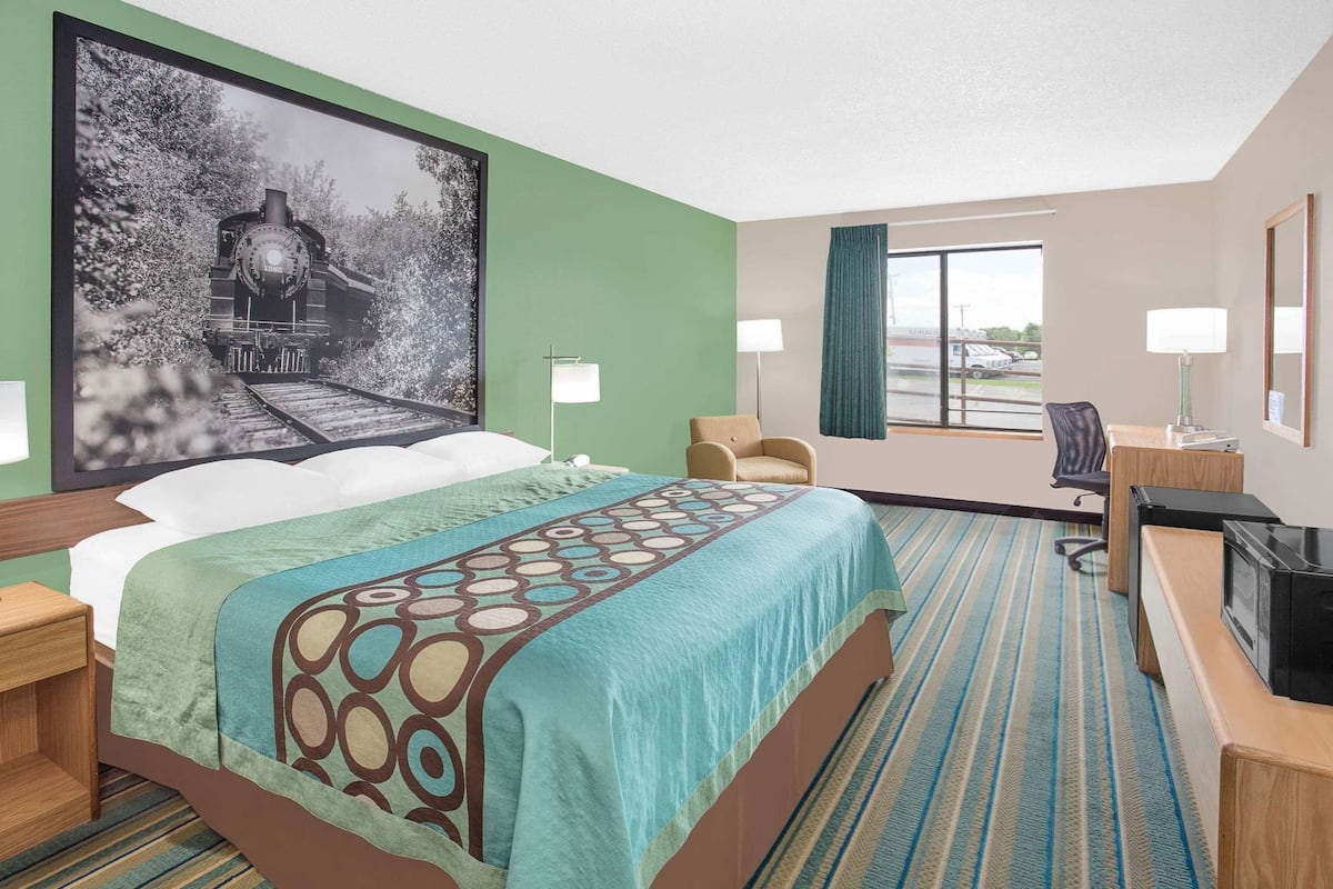 A hotel room with a large bed, two bedside tables, a desk with a chair, a large window, and a wall-mounted TV.