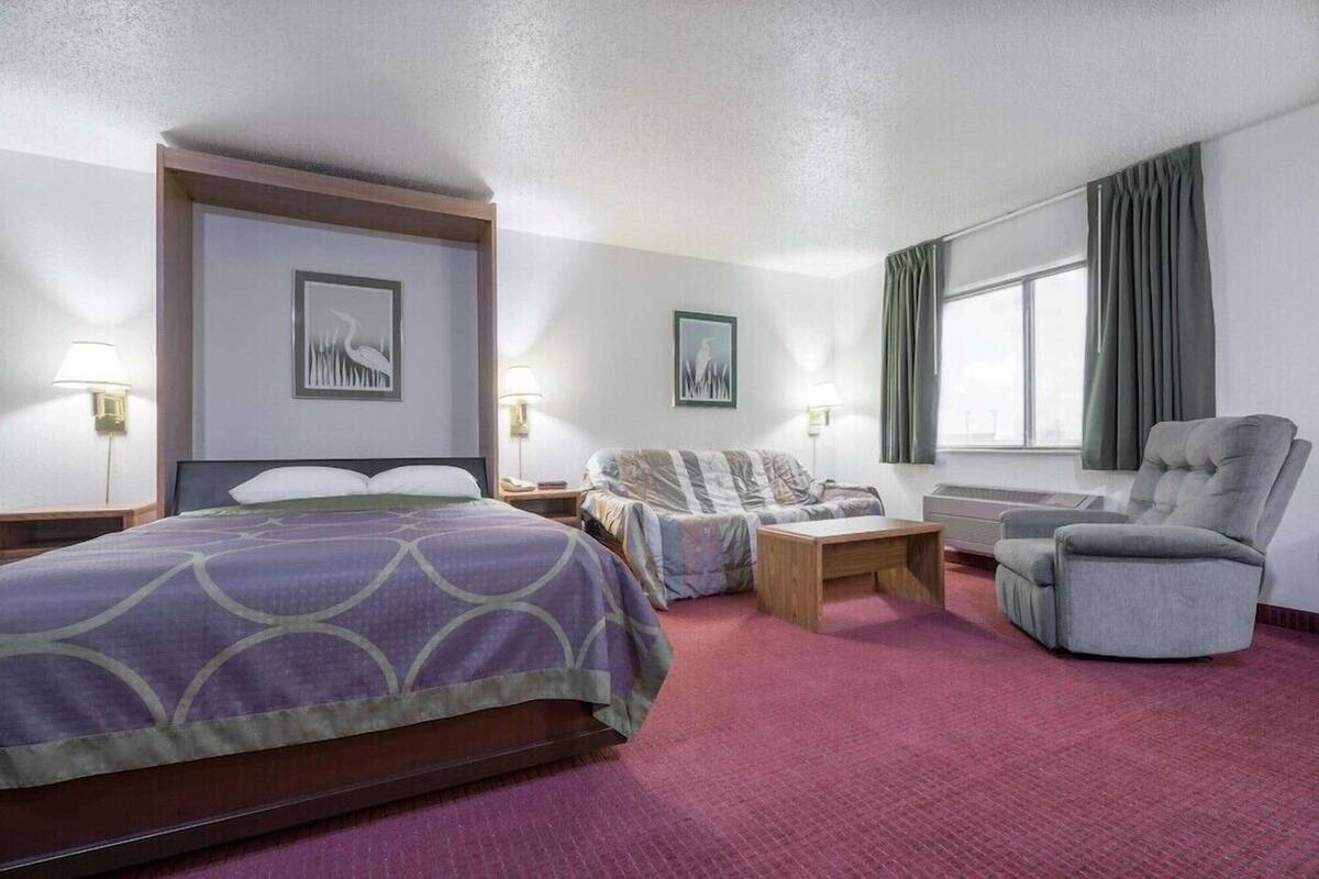 Een hotelkamer met een bed, een bank, een stoel, een bureau en een raam met gordijnen.