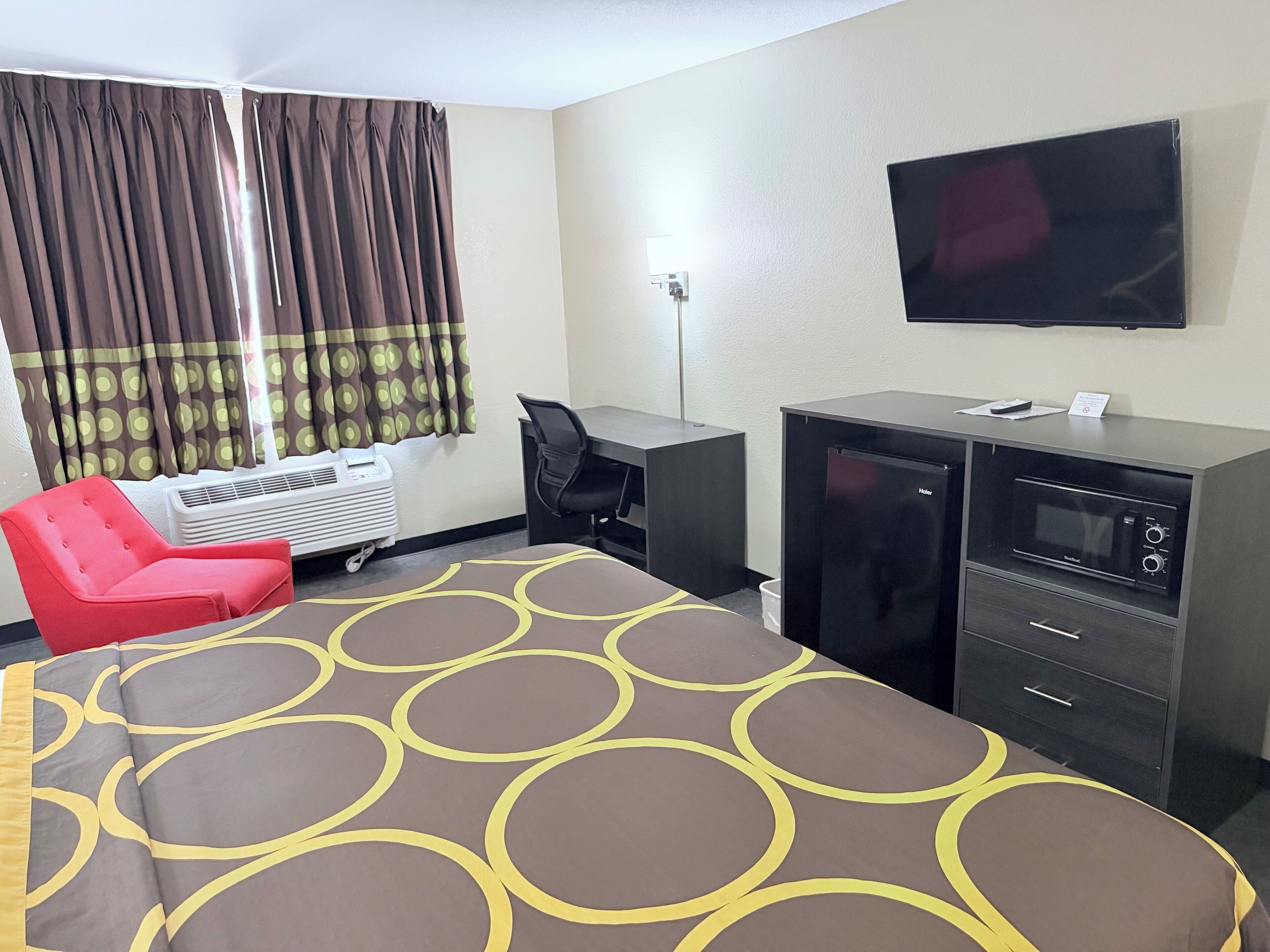 A hotel room with a bed, a desk, a chair, a television, and a kitchenette.