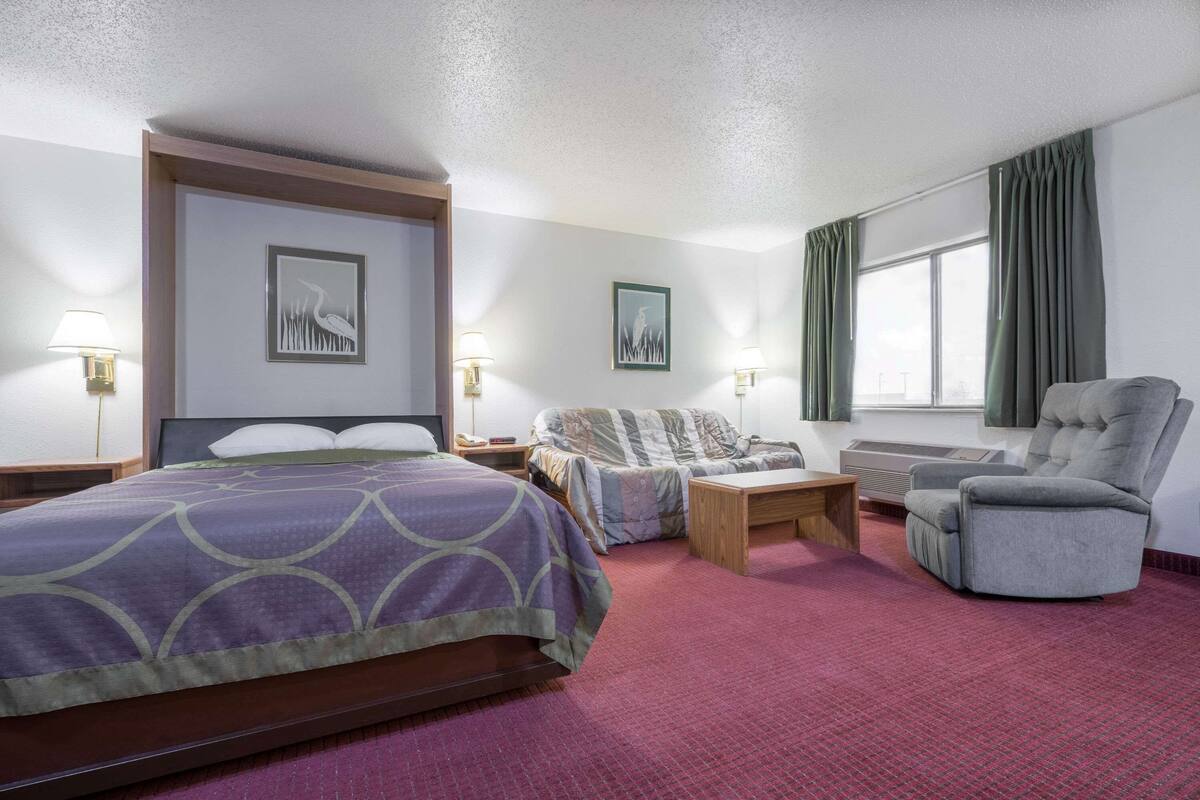 Een hotelkamer met een bed, een stoel, een bureau en een raam met gordijnen.