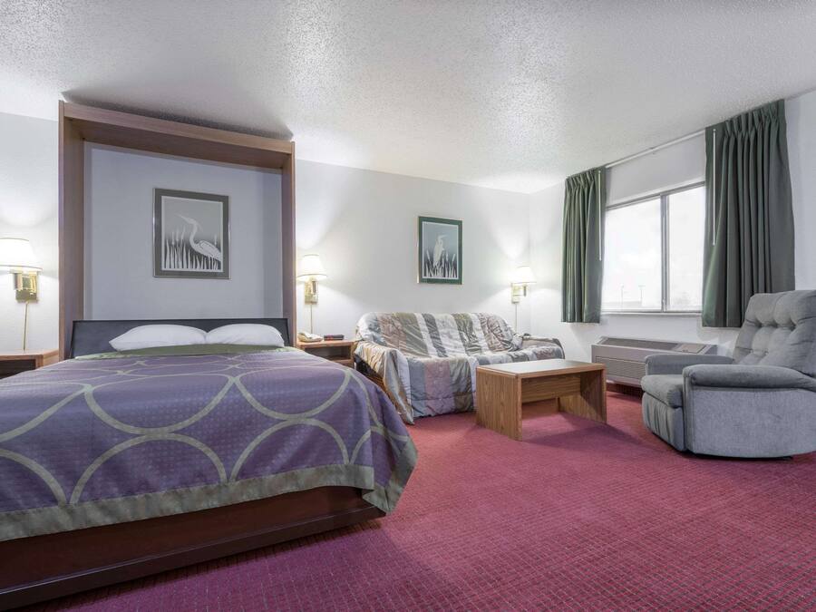 A hotel room with a bed, a chair, a desk, and a window with curtains.