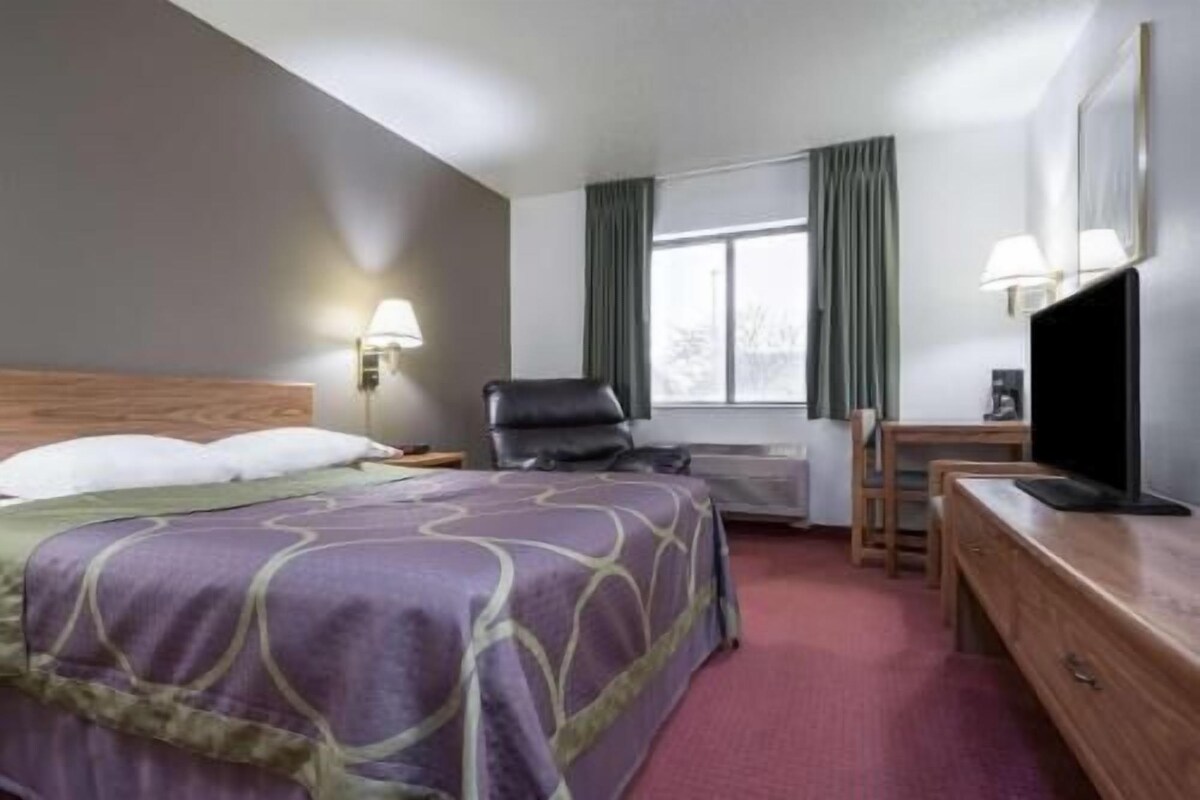 Habitació d'hotel amb llit, escriptori, cadira, televisió i finestra amb cortines.