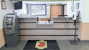 Un espace d’accueil comprenant un comptoir de réception, un distributeur automatique de billets, un distributeur de gel hydroalcoolique et le logo de la chaîne Super 8 by Wyndham sur le tapis d’entrée.