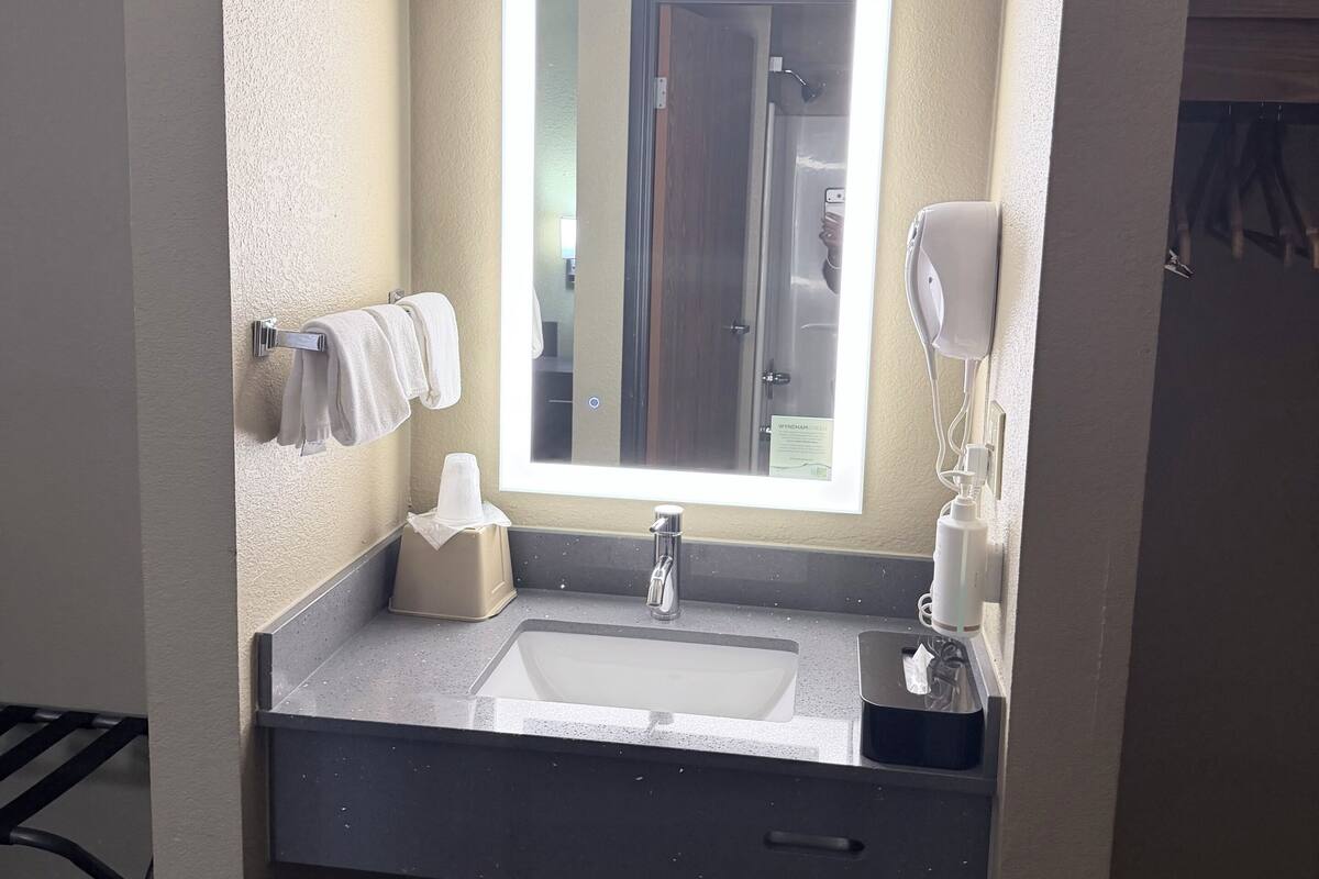 Een badkamer met een wastafel, spiegel, zeepdispenser en prullenbak.