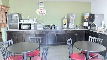 A kitchen with a clock, a Superstart breakfast sign, a microwave, toaster, coffee machine, and a juice dispenser.