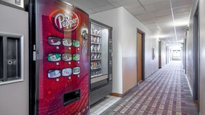 Un couloir avec des distributeurs automatiques, un sol recouvert de moquette et des portes de part et d’autre.