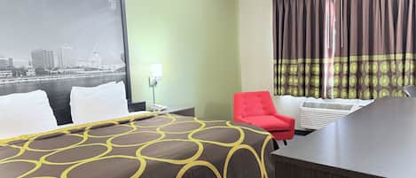 Una habitación de hotel con cama, escritorio, silla, mesita de noche, lámpara y ventana con cortinas.